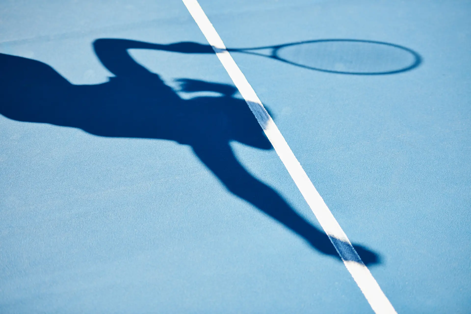 Tennisspielerin als Schattenwurf auf blauem Hartplatz